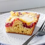 A slice of coffee cake with a layer of fruit filling and cream cheese on a white plate, next to a fork.