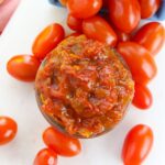 A jar of jam next to tomatoes.