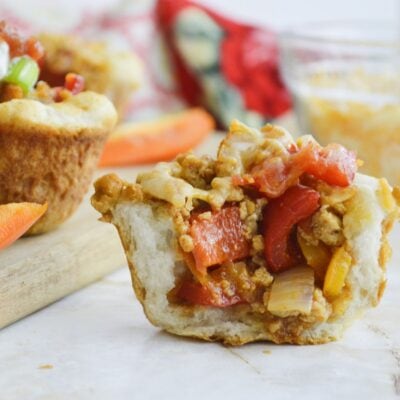 A close-up of a stuffed bread cup filled with seasoned ground meat, diced red and yellow bell peppers, and onions on a light surface.