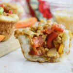 A biscuit cup filled with cooked ground meat, diced red bell peppers, and onions, shown cut in half on a light surface.
