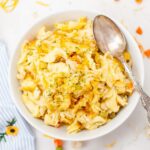 A bowl of creamy chicken noodle casserole topped with shredded cheese and herbs, with a spoon on the side.