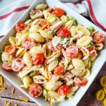 A bowl of pasta salad with shell noodles, cherry tomatoes, lettuce, shredded cheese, and bacon pieces, mixed with a creamy dressing.