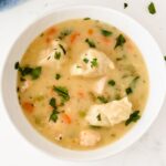 A bowl of creamy chicken and dumplings soup with diced carrots, celery, and parsley garnish.