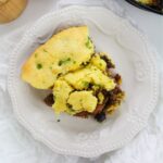 A serving of cornbread casserole with ground meat and herbs on a white decorative plate.