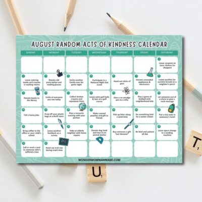 A calendar titled "August Acts of Kindness Calendar" lies on a white surface, surrounded by pencils and wooden letter tiles. Each day features a unique act from the august acts of kindness calendar to inspire daily goodwill.