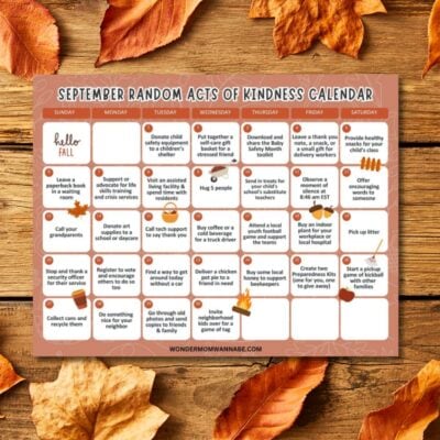 A September acts of kindness calendar featuring daily suggestions for kind actions, displayed on a wooden surface with scattered autumn leaves around the edges.