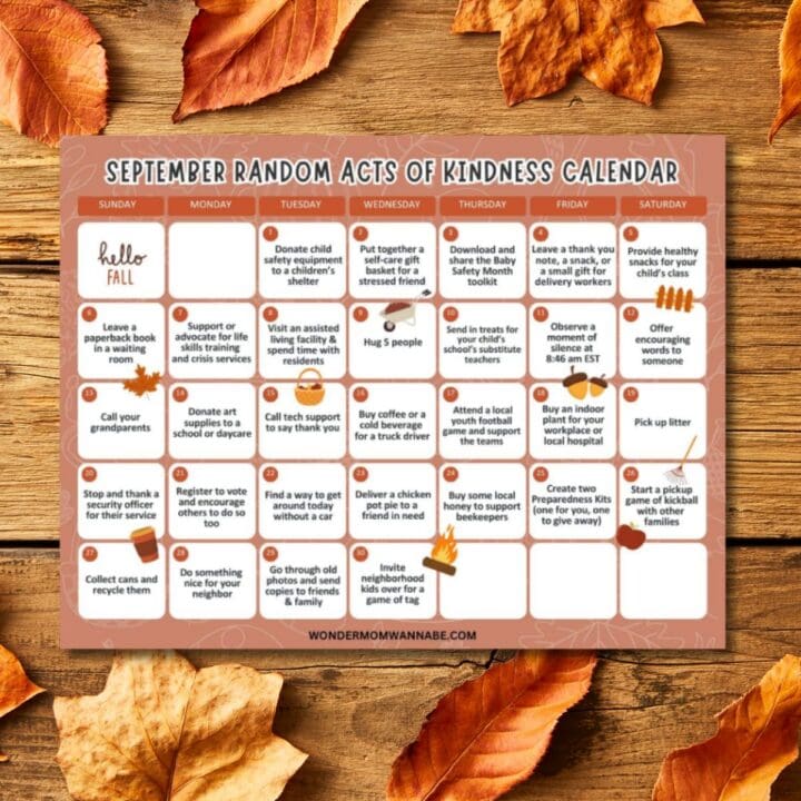 A September acts of kindness calendar featuring daily suggestions for kind actions, displayed on a wooden surface with scattered autumn leaves around the edges.